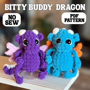 May include: Two crocheted dragon toys, one purple and one blue, with large black eyes and small wings. The purple dragon has pink wings, and the blue dragon has orange wings. The text "BITTY BUDDY DRAGON" is at the top, with "NO SEW" and "PDF PATTERN" in boxes.