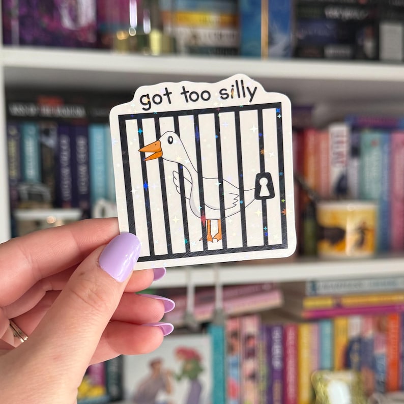 Op de afbeelding: Een witte gans met een zwarte snavel zit gevangen in een kooi met de tekst "got too silly" erop. De kooi is gemaakt van zwarte tralies en heeft een sleutelgat aan de rechterkant. De achtergrond is een boekenkast met boeken.