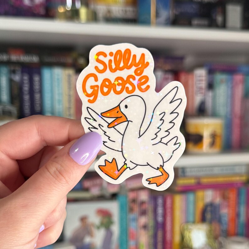 Op de afbeelding: Een witte sticker met een cartoon-gans en de tekst "Silly Goose" in oranje glitter.