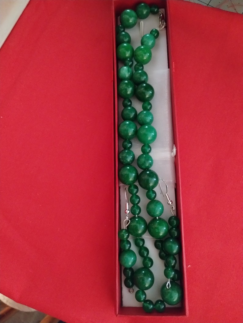 May include: A green jade necklace and earrings set in a red box. The necklace is made of large, round beads and the earrings are simple studs.