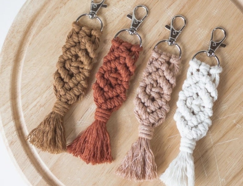 May include: Four handmade macrame keychains with tassels in brown, orange, pink, and white.