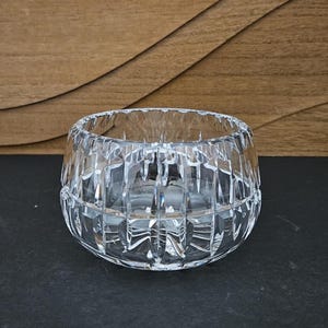 May include: A clear, cut-glass bowl with a rounded shape. The bowl features a geometric pattern of vertical and horizontal cuts, creating a textured surface. The bowl is designed to hold small items or serve as a decorative piece.