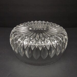 May include: A clear, round glass bowl with a detailed, cut-glass pattern. The bowl features a central, flower-like design surrounded by radiating, leaf-shaped cuts. The rim has a scalloped edge, and the bowl sits on a dark surface.