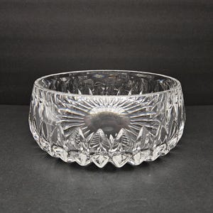 May include: A clear, cut-glass bowl with a circular form. The bowl has a sunburst design on the base and detailed patterns around the sides. The bowl is likely for serving or display.