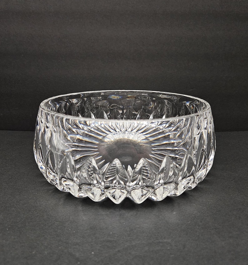 May include: A clear, cut-glass bowl with a circular form. The bowl has a sunburst design on the base and detailed patterns around the sides. The bowl is likely for serving or display.