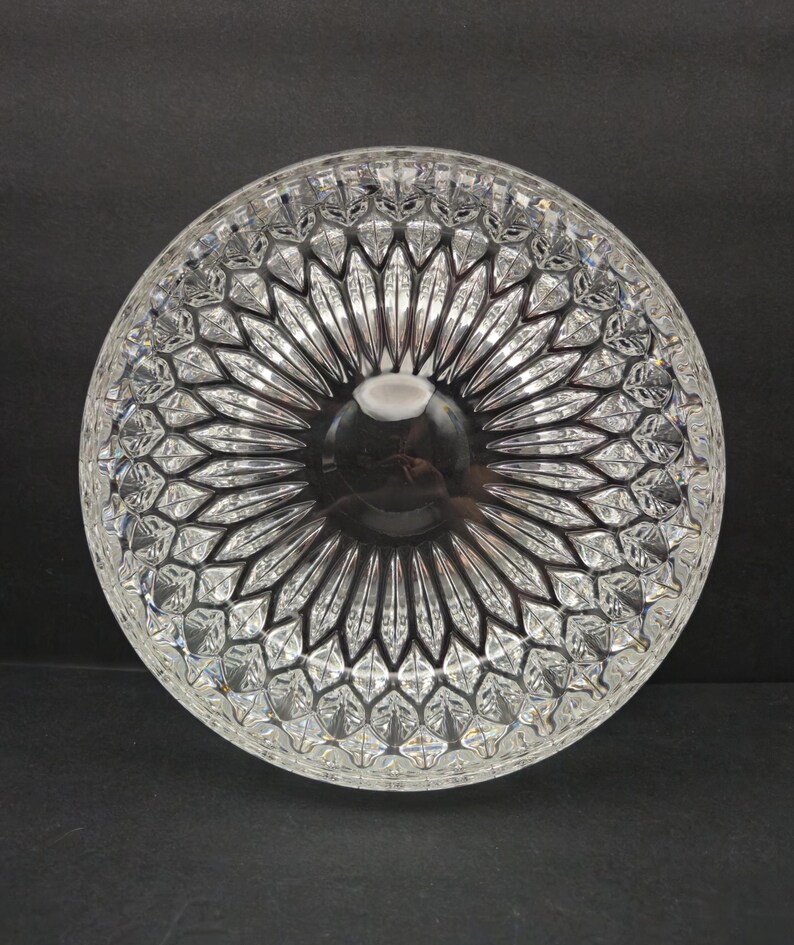 May include: A clear, circular glass bowl with an intricate geometric design. The bowl has a central indentation and radiating lines, forming a starburst pattern. This decorative bowl is likely for serving or display.