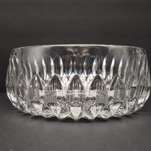 May include: A clear glass bowl with a textured design. The bowl has a wide opening and a series of pointed, petal-like shapes around the base. The glass is transparent, allowing light to pass through. The bowl is likely for decorative use.