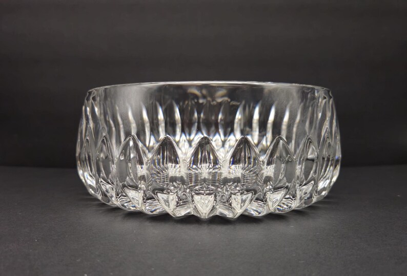 May include: A clear glass bowl with a textured design. The bowl has a wide opening and a series of pointed, petal-like shapes around the base. The glass is transparent, allowing light to pass through. The bowl is likely for decorative use.