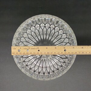 May include: Clear glass serving bowl with a detailed, geometric pattern. The bowl is round and measures approximately 23 cm in diameter. A wooden ruler is placed across the bowl for measurement.