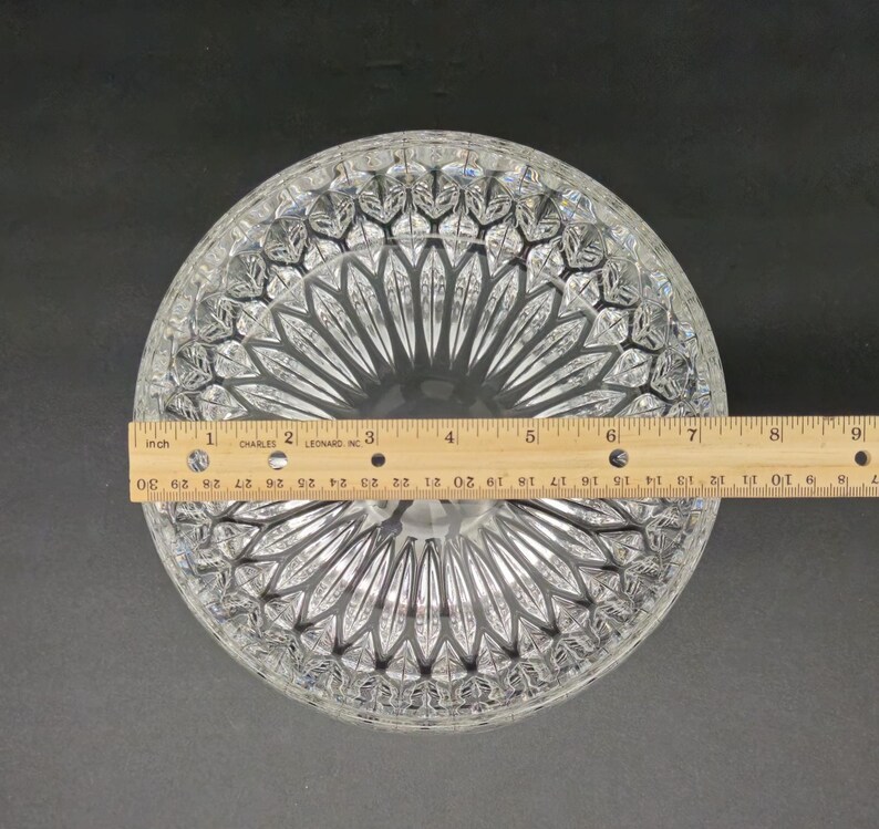 May include: Clear glass serving bowl with a detailed, geometric pattern. The bowl is round and measures approximately 23 cm in diameter. A wooden ruler is placed across the bowl for measurement.