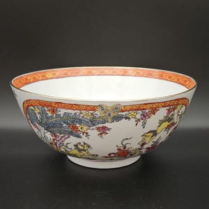 May include: A white porcelain bowl with a red and gold rim. The bowl is decorated with a floral pattern and a scene of a mythical creature.