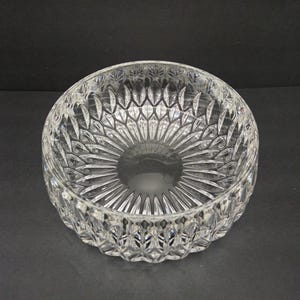 May include: A clear crystal bowl with detailed cut patterns. The bowl has a circular base and radiating lines, creating a starburst effect. The rim features a repeating diamond design. The bowl is approximately 20 cm in diameter.
