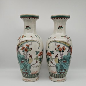 Puede incluir: Dos jarrones de cerámica a juego con fondo crema. Cada jarrón presenta una pintura detallada de pájaros, flores y follaje en tonos rojos, verdes y azules. Los bordes están adornados con una banda verde.