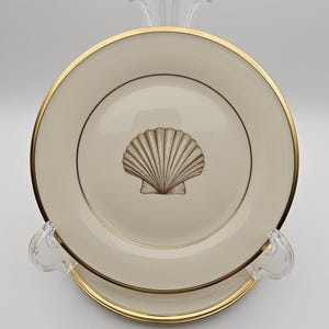 May include: A white ceramic plate with a gold rim and a gold seashell design in the center.