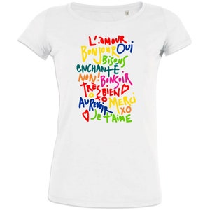 May include: White t-shirt with a colorful handwritten design. The design includes phrases like "L'AMOUR", "BONJOUR", "MERCI", and "JE T'AIME" in various colors. The shirt has a crew neck and short sleeves.