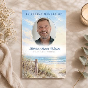 May include: A rectangular memorial card featuring a portrait of a smiling man in an oval frame, with the text IN LOVING MEMORY OF, Robert James Wilson, and the dates 12 MARCH 1962 - 6 OCTOBER 2026 over a beach and ocean scene.