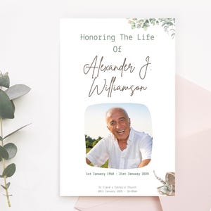 May include: A white memorial card with a green leafy border. The card honors the life of Alexander J. Williamson. It includes a photo of a man smiling, the dates January 1, 1948 to January 21, 2025, and information about a Catholic church service.