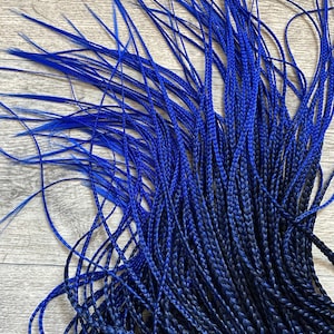 Peut inclure: Gros plan sur des extensions de cheveux tressés bleus. Les cheveux passent d'un bleu roi vibrant aux pointes à une nuance plus foncée, presque marine, aux racines. Les tresses sont étroitement tissées, créant un aspect texturé.