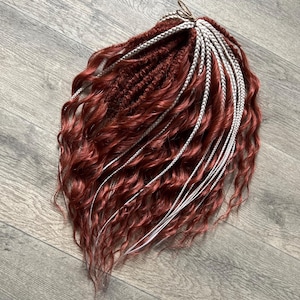 May include: A bundle of reddish-brown synthetic dreadlocks with wavy texture and white accent braids. The dreadlocks are arranged in a cluster, showcasing a blend of colors and styles. The hair extensions are designed for versatile styling options.