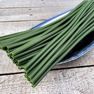 May include: A bundle of green plastic drinking straws, arranged in a fan shape on a silver platter. The straws are all the same size and are made of a flexible material.