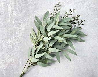 May include: A bunch of artificial greenery with long, slender leaves and small green buds. The leaves are a light green color and have a slightly textured surface.