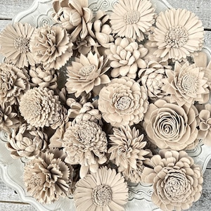May include: A collection of beige wooden sola flower heads in various shapes and sizes arranged on a white plate. The flowers are made of natural wood and have a rustic, farmhouse aesthetic.