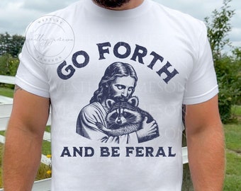 May include: White t-shirt with a blue graphic of Jesus holding a raccoon. The text "Go Forth and Be Feral" is printed below the image.