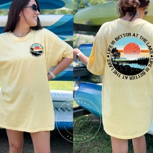 May include: A yellow t-shirt with a graphic print of a sunset over a lake. The text "Life is better at the lake" is printed around the graphic. The text "Westley Jameson" is printed on the back of the shirt.