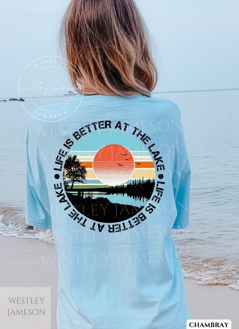 May include: A light blue t-shirt with a circular graphic design featuring a sunset over a lake with trees and the text "Life is better at the lake".