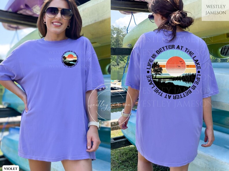 May include: A purple t-shirt with a graphic of a sunset over a lake and the text "Life is better at the lake" in a circle. The text "Westley Jameson" is printed on the back of the shirt.