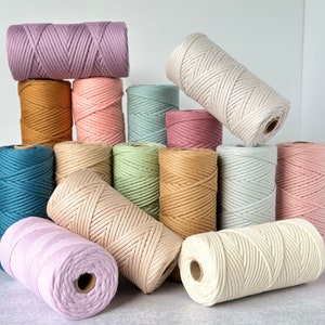 May include: A collection of colorful macrame cord spools in various pastel shades, including lavender, peach, teal, and cream. The spools are arranged in a visually appealing display, showcasing the different colors and textures of the cord.