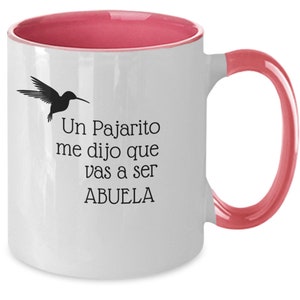 May include: White ceramic coffee mug with a pink rim and handle. The mug features a black silhouette of a hummingbird and the text "Un Pajarito me dijo que vas a ser ABUELA".