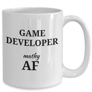 May include: White ceramic coffee mug with black text that reads "GAME DEVELOPER mathy AF".