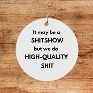 May include: White round Christmas ornament with black text that reads "It may be a SHITSOW but we do HIGH-QUALITY SHIT".