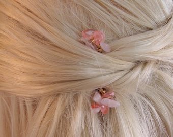 May include: Two pink and white gemstone hair clips with gold wire accents. The clips are in blonde hair.