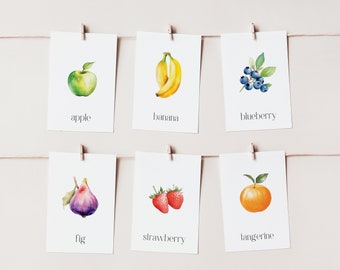 Puede incluir: Seis ilustraciones de acuarela de diferentes frutas y bayas en tarjetas blancas con el nombre de cada fruta escrito debajo de la imagen. Las frutas son una manzana, un plátano, un arándano, un higo, una fresa y una mandarina.