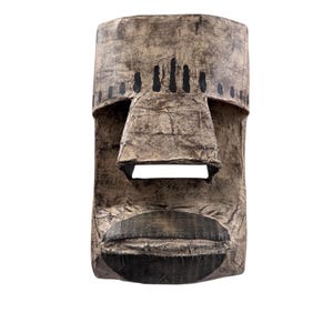 May include: A handcrafted mask with a textured, aged look. The mask has a rectangular form with a pronounced nose and mouth, and small, dark circular and vertical markings. The color scheme is mainly brown and black tones.
