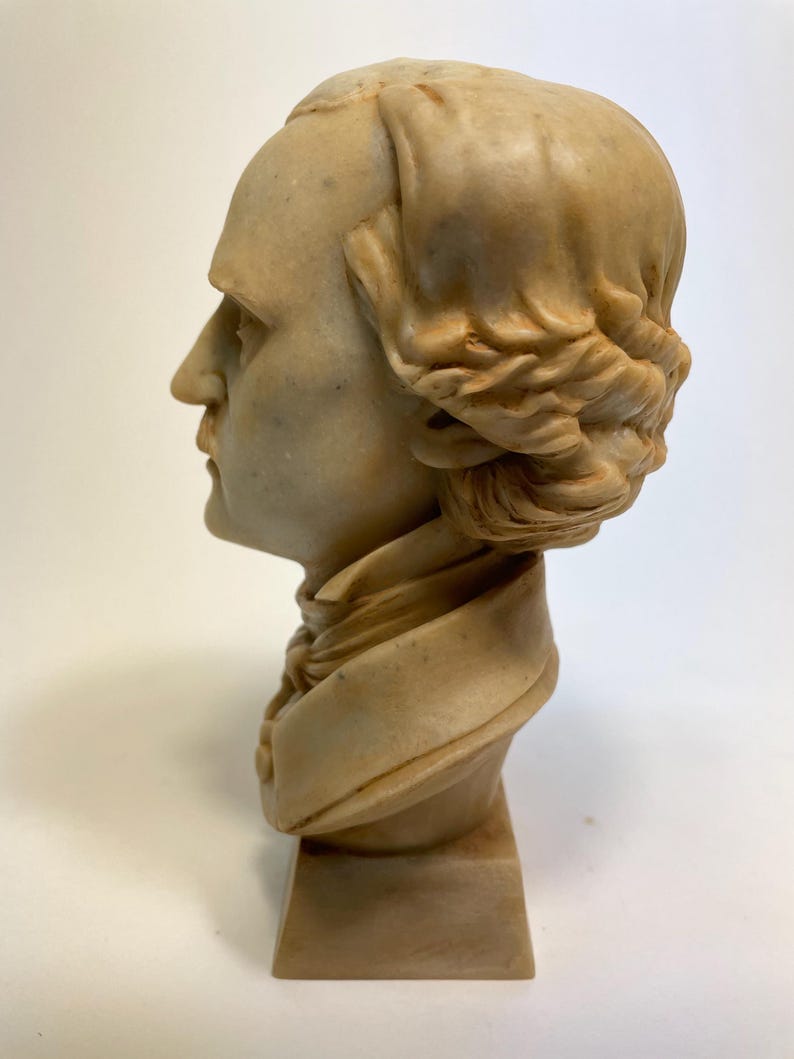 May include: A beige bust sculpture of a person with a braided hairstyle. The bust is on a beige pedestal.