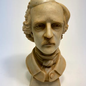 May include: A white ceramic bust of a man with a mustache and a cap. The bust is on a white base.