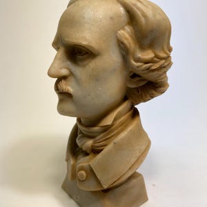 May include: A beige marble bust sculpture of a man with short, wavy hair. The bust is on a square base.