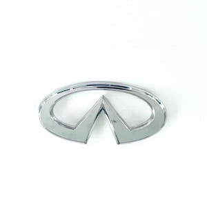 May include: A silver Infiniti car emblem with a rounded oval shape and a pointed, triangular center.