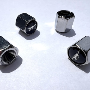 Puede incluir: Cuatro tapones de válvula de neumático plateados. Dos tapones tienen una cara negra con un emblema de caballo blanco. Los otros dos tapones son plateados, de forma hexagonal y con rosca interior.