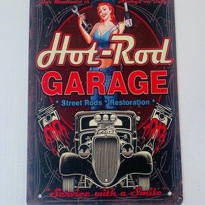 Puede incluir: Un letrero de metal de estilo vintage con un esquema de color rojo, blanco y azul. Presenta a una chica pin-up sosteniendo herramientas y un coche hot rod con llamas. El texto dice "Our Mechanic is Always on Duty", "Hot-Rod Garage", "Street Rods Restoration" y "Service with a Smile".