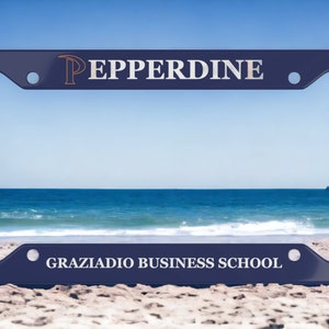 May include: A blue license plate frame with the text "Pepperdine" and "Graziadio Business School" on it. The frame is on a sandy beach with a blue ocean in the background.
