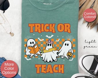 May include: Light green t-shirt with a graphic of three ghosts. The ghosts are holding a book, a pencil, and a pumpkin. The text "Trick or Teach" is printed on the shirt.