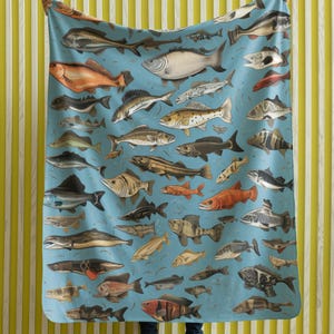 May include: A blue throw blanket with a colorful pattern of various fish species. The blanket is made of soft, comfortable fabric and features a variety of fish, including tuna, salmon, and trout.