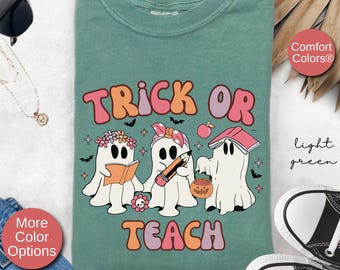 May include: Light green t-shirt with a graphic of three ghosts dressed as teachers. The text "Trick or Teach" is printed in pink and purple letters.