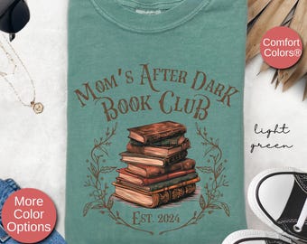 May include: A light green t-shirt with the text "Mom's After Dark Book Club" in brown lettering. The shirt features a stack of vintage books with a floral design around them. The text "Est. 2024" is below the books.