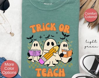 May include: A light green t-shirt with a graphic of three ghosts holding books and a pencil. The text "Trick or Teach" is printed in orange and yellow letters.