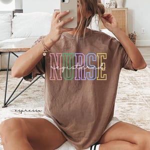 Pode incluir: Uma camiseta marrom com a palavra "NURSE" em letras coloridas e a palavra "registered" escrita em cursiva abaixo.